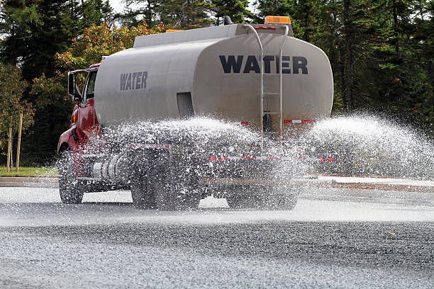 Water tank truck spraying water on a new road construction site in preparation for paving.